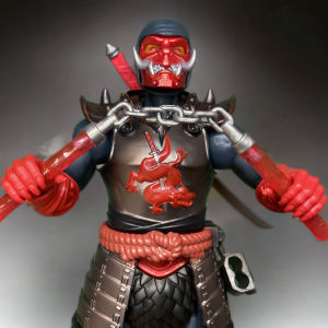 Detailed view of Ninjor’s dragon-themed nunchucks with translucent red handles, secured in a belt holder, displayed alongside the figure’s chain mail skirt.