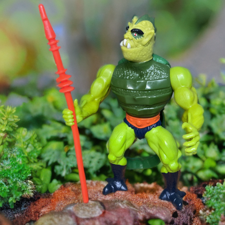 Eine alte Whiplash-Actionfigur aus dem Jahr 1984 mit grünen Schuppen, Stachelpanzerung und einem gefederten Schwanz, die mit einem Speer vor einem Retro-MOTU-Hintergrund posiert.