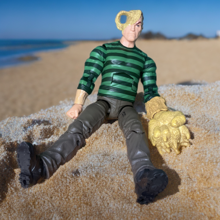 La figurine Sandman 2025 est posée dans une position défensive avec des accessoires de poing de sable, entourée de pièces à effet de sable sur un présentoir rétro sur le thème de Spider-Man.