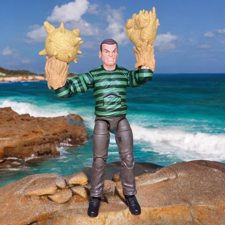 Gros plan sur le torse musclé à la texture sable et la chemise à rayures vertes de la figurine Sandman Retro 2025, mettant en valeur sa sculpture et sa peinture détaillées.