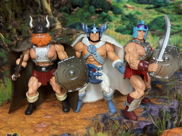 Uma ilustração de Magnon, um nobre herói de armadura, enfrentando Barbaros, um guerreiro caótico com um machado, e Huk, uma figura inspirada em Vikings com barba ruiva, contra o portal místico Well of Secrets (Poço dos Segredos) que liga Ferror ao universo Legends of Dragonore.