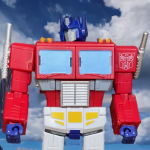 A Studio Series 86-31 Optimus Prime figure in robot mode with a red and blue color scheme and a trailer in the background.