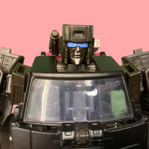 Trailbreaker’s robot mode holding the blaster hand accessory, posed in a defensive stance on a desert landscape, with the backpack slightly raised to make the shoulder gadgets more prominent.