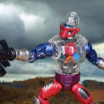 Masterverse New Eternia Roboto: A Robotic Marvel Unveiled Uma figura de ação de 7 polegadas do Masterverse New Eternia Roboto está em uma pose dinâmica, mostrando sua cabeça e torso transparentes com engrenagens visíveis, viseira roxa e acessório de braço blaster vermelho.