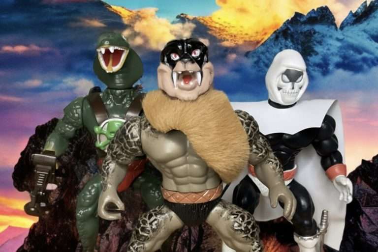 King Kobra, Wolf Warrior e Skull Man se reuniram em uma plataforma rochosa com montanhas ao pôr do sol.