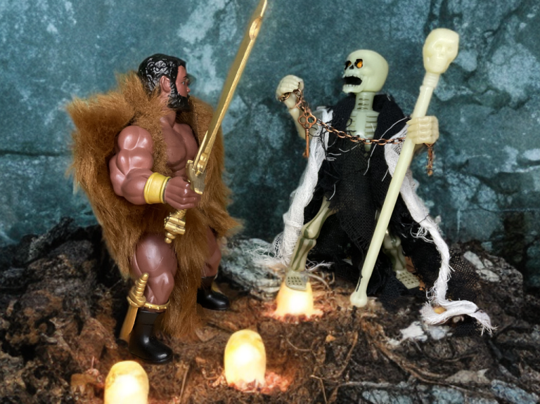 Archterrus, um esqueleto verde pálido com um manto esfarrapado, levanta seu cajado em uma caverna brilhante contra Hércules, que balança uma espada dourada, em uma cena dramática de sessão de fotos do Zoloworld.