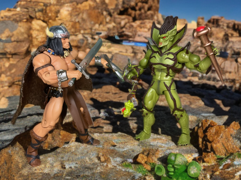 Vikor charging at Evil Seed with axe raised, Evil Seed countering with staff, in a desert setting with scattered debris.