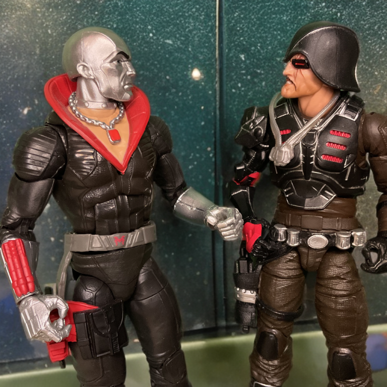 In a teal-lit room, Destro, in a black uniform with a red collar and silver chain, shakes hands with Major Bludd, in a dark tactical outfit with red accents and a hooded helmet. The reflective backdrop enhances the tense, strategic atmosphere of their exchange.