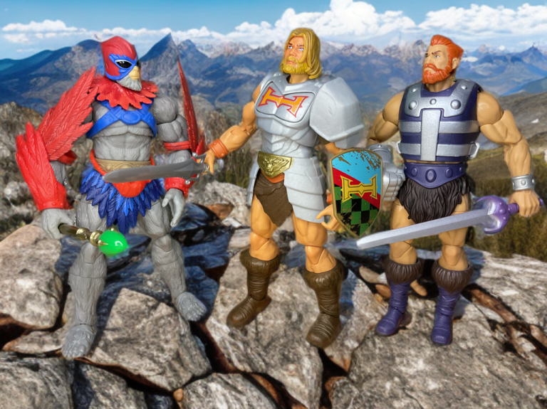 Die Actionfiguren Stratos, He-Man und Fisto stehen auf einem felsigen Hügel mit einer malerischen Bergkette im Hintergrund.