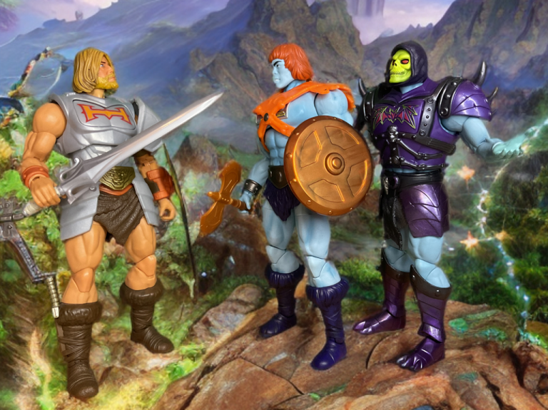 Die Actionfiguren He-Man, Faker und Skeletor stehen auf einem Felsvorsprung vor einer fantastischen Kulisse.