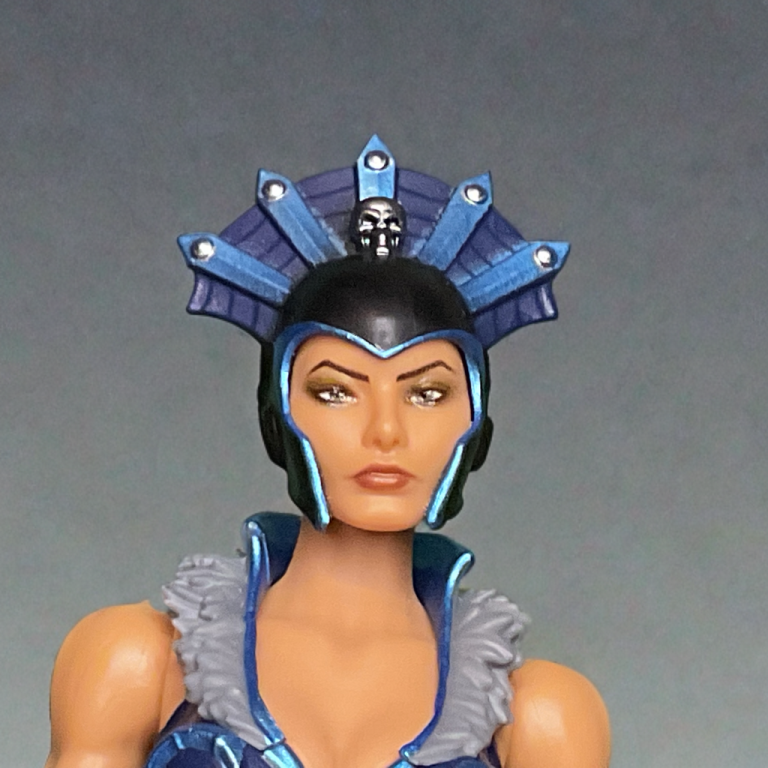Nahaufnahme der New Eternia Evil-Lyn-Actionfigur. Hervorzuheben sind ihr detaillierter Totenkopfhelm mit Spinnennetzmuster und ihr abnehmbarer Umhang aus Weichware.