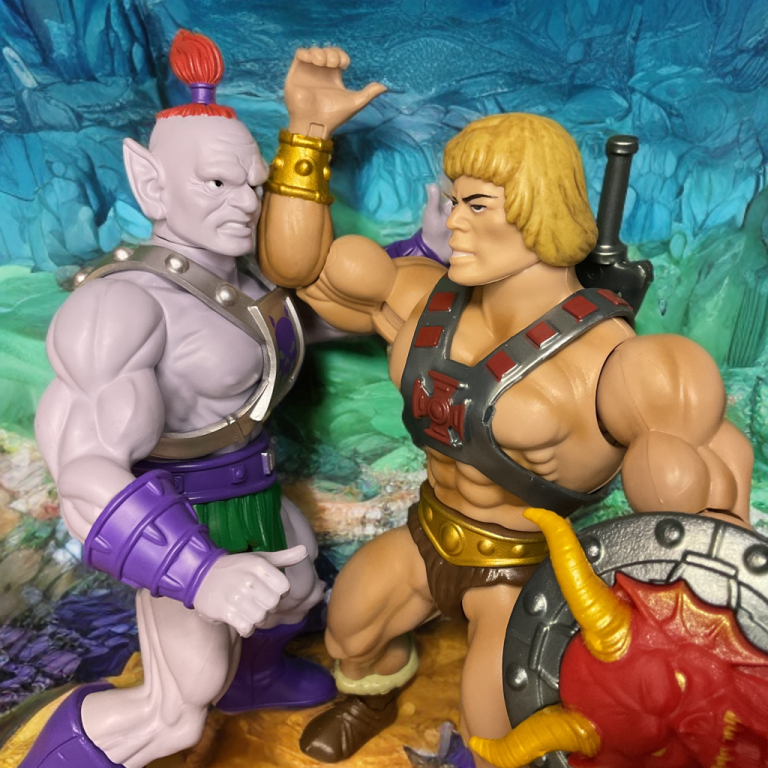 Action-packed scene of He-Man mid-swing clashing against Baltard.