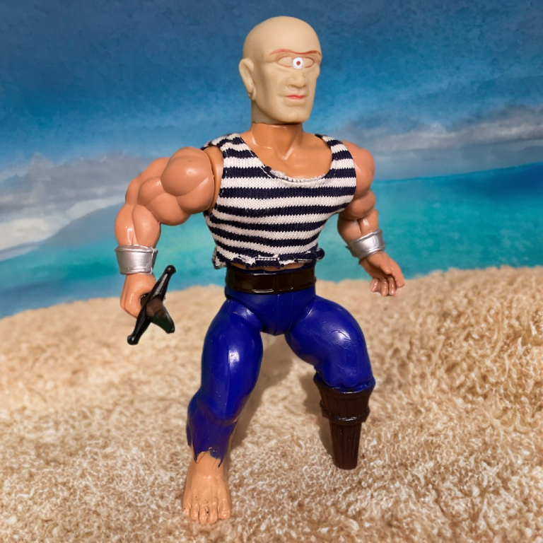 On a sunlit beach with turquoise waters, Pegleg, a bald pirate with a third eye on his forehead, stands in a striped black-and-white shirt and blue pants, his right leg a weathered peg leg. He holds a dagger low, with silver cuffs on his arms and one bare foot on soft sand.