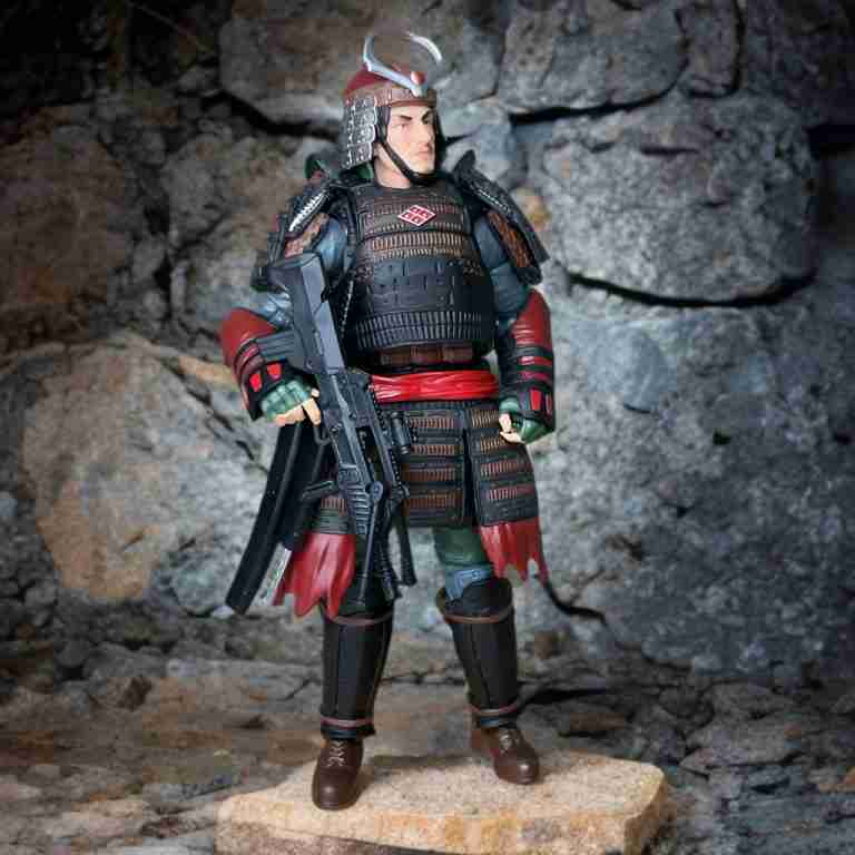 Uma foto de Budo do G.I. Joe Classified #174 com armadura de samurai completa, posando com um tanto e um nodachi, em um cenário de pedra.