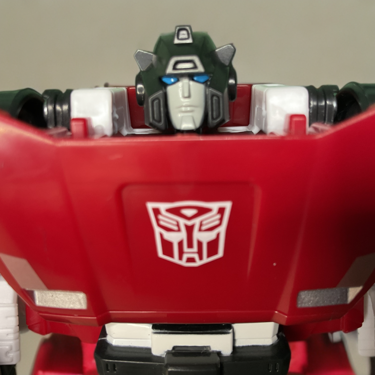 Close-up da escultura da cabeça e da insígnia de Sideswipe, destacando detalhes em cel-shaded inspirados no videogame de 2015.