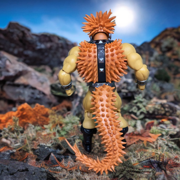 A 5.5-inch Spikor action figure with brown, spiky armor and a detachable tail stands on a rocky display. The packaging features a black-and-white sketch of Spikor lunging, with amber spikes and lore text.
