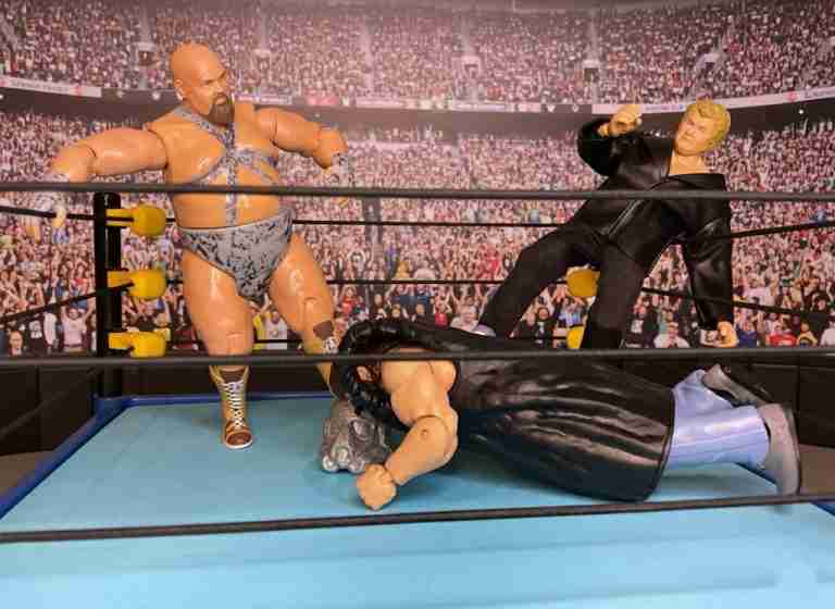 Bastion Booger und Harley Race Action-Figuren stampfen auf einem am Boden liegenden Shockmaster im Ring herum, während die Menge im Hintergrund jubelt.