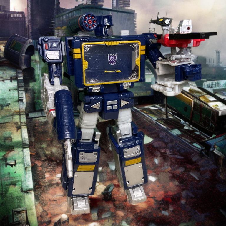 Blue and silver Soundwave robot toy standing in a dilapidated city scene with green haze, holding a blaster and shoulder turret, posed dynamically.