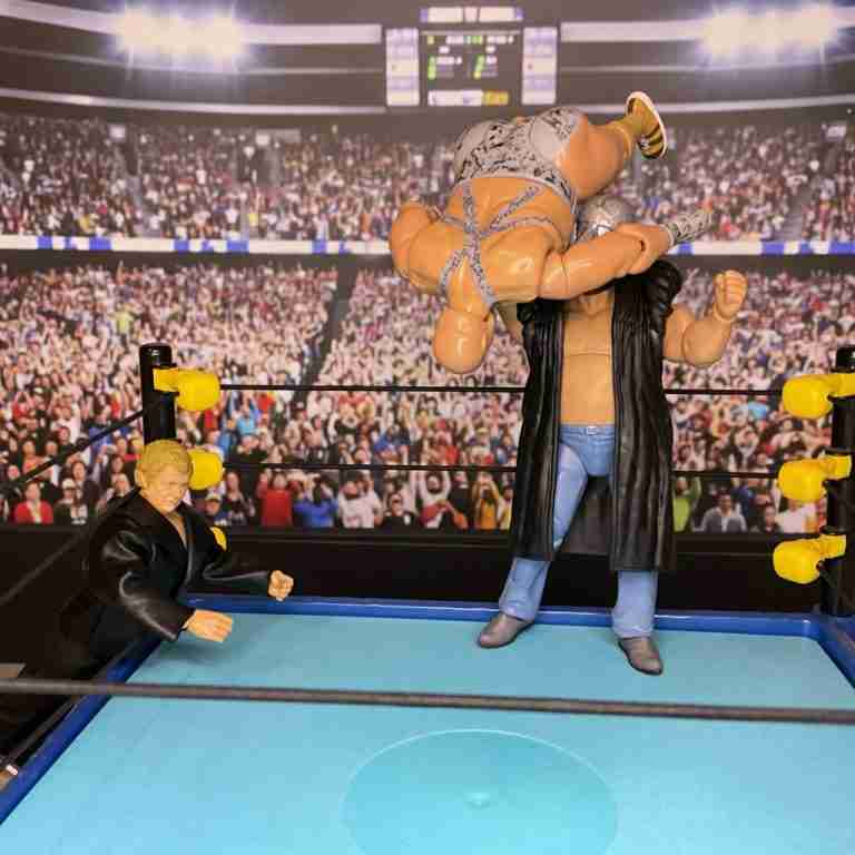 Die Shockmaster-Actionfigur hebt Bastion Booger hoch und knallt ihn auf die Ringmatte, während Harley Race zusieht.