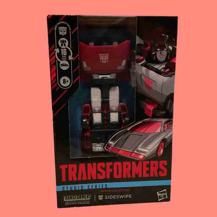 Figura embalada com fundo neutro, exibindo o modo robô em cores vibrantes de vermelho e prata.