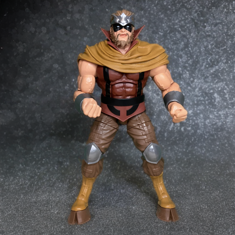 Full-length shot of Gorgon standing tall – thick Hercules-buck torso, brown and orange costume, headband, and massive cloven hooves.